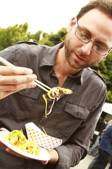 Andrew at a food blogging conference, eating some tasty samples with chopsticks.