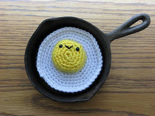 Overhead view of a cast iron skillet with a crocheted fried egg.