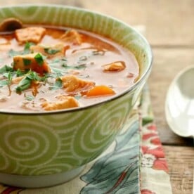 A green bowl with chicken and tomato soup.