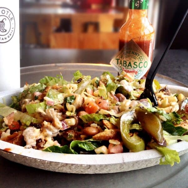 A Chipotle bowl piled with lettuce, chicken, pinto beans, corn and tomato salsas, cheese, and sour cream.