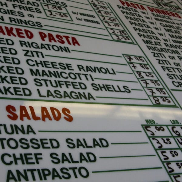 A crowded menu board of baked pastas and salads, with prices but no nutrition information to help you choose.